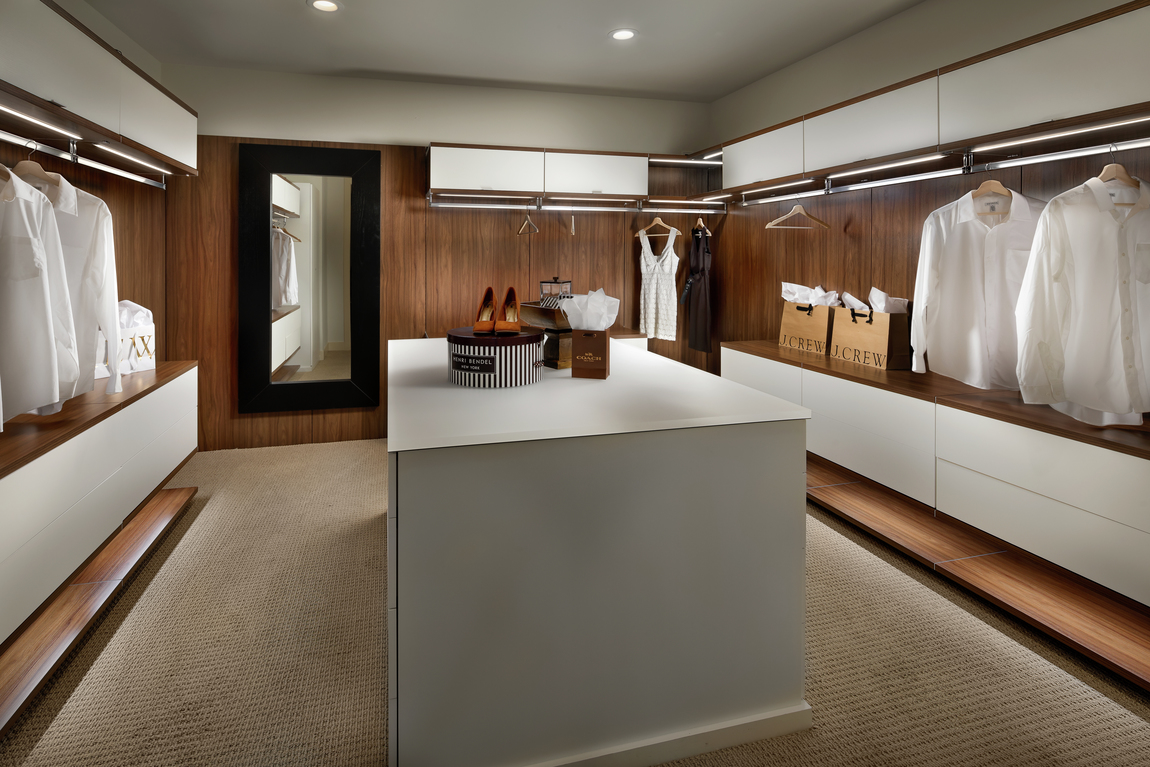 Modern closet with white center island and carpeting with plenty of hanging space.