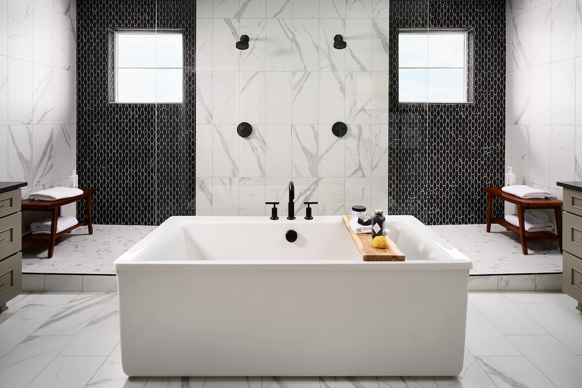 White tile bathroom with black accent walls in shower and standing center soaking tub. 