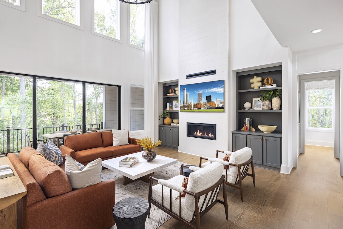 Luxury living room with burnt orange sofa and white chairs, two-story space with matte black sliding glass doors. 