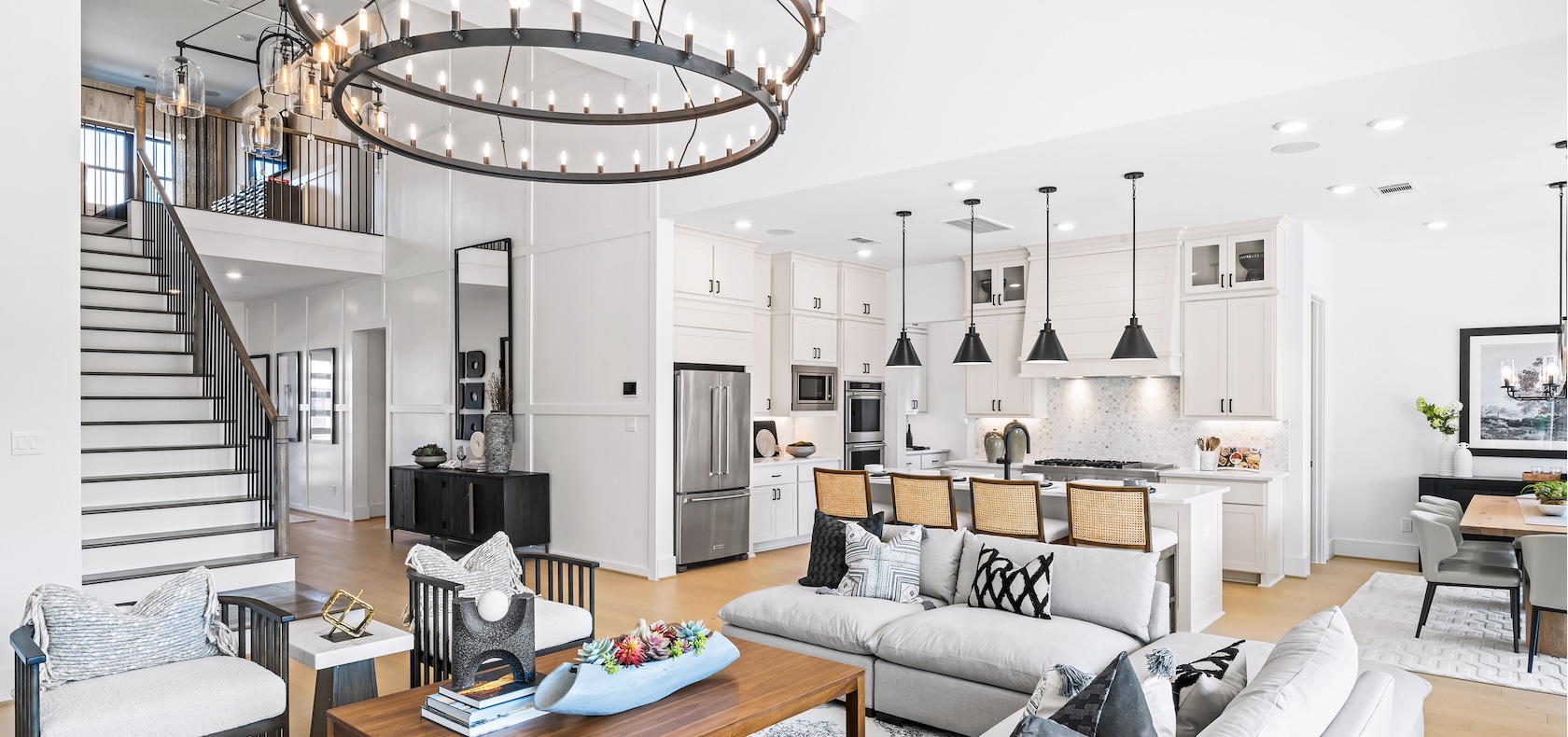 Luxury home design featuring living room with circular double-tiered chandelier and white kitchen cabinets with hard wood flooring.