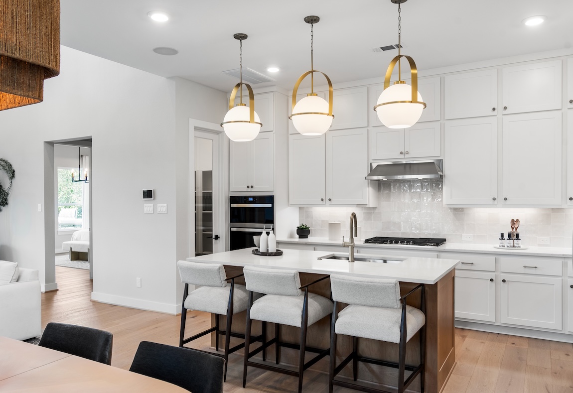 Luxury kitchen with white cabinets, paint color with brown island featuring white quartz countertop and white chairs with matte black accents. 