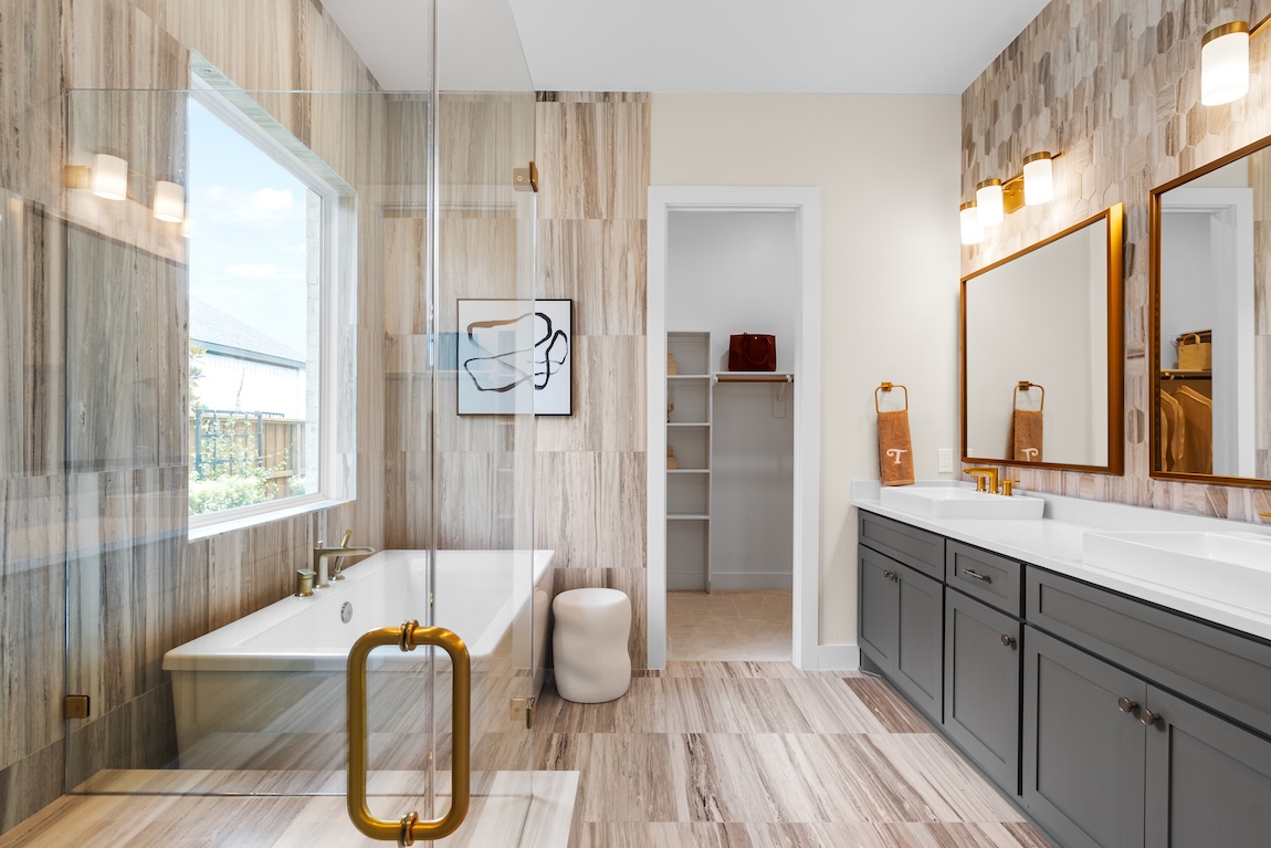 Luxury bathroom design with gold-rimmed mirror, scones, and glass shower with bathtub. 